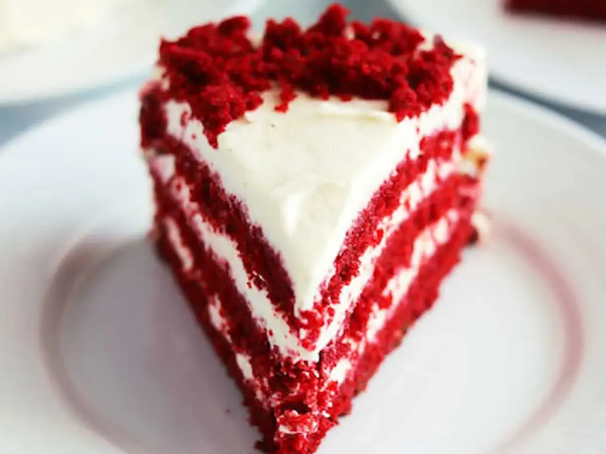 En bit saftig red velvet-tårta med krämig frosting och smulor på toppen.