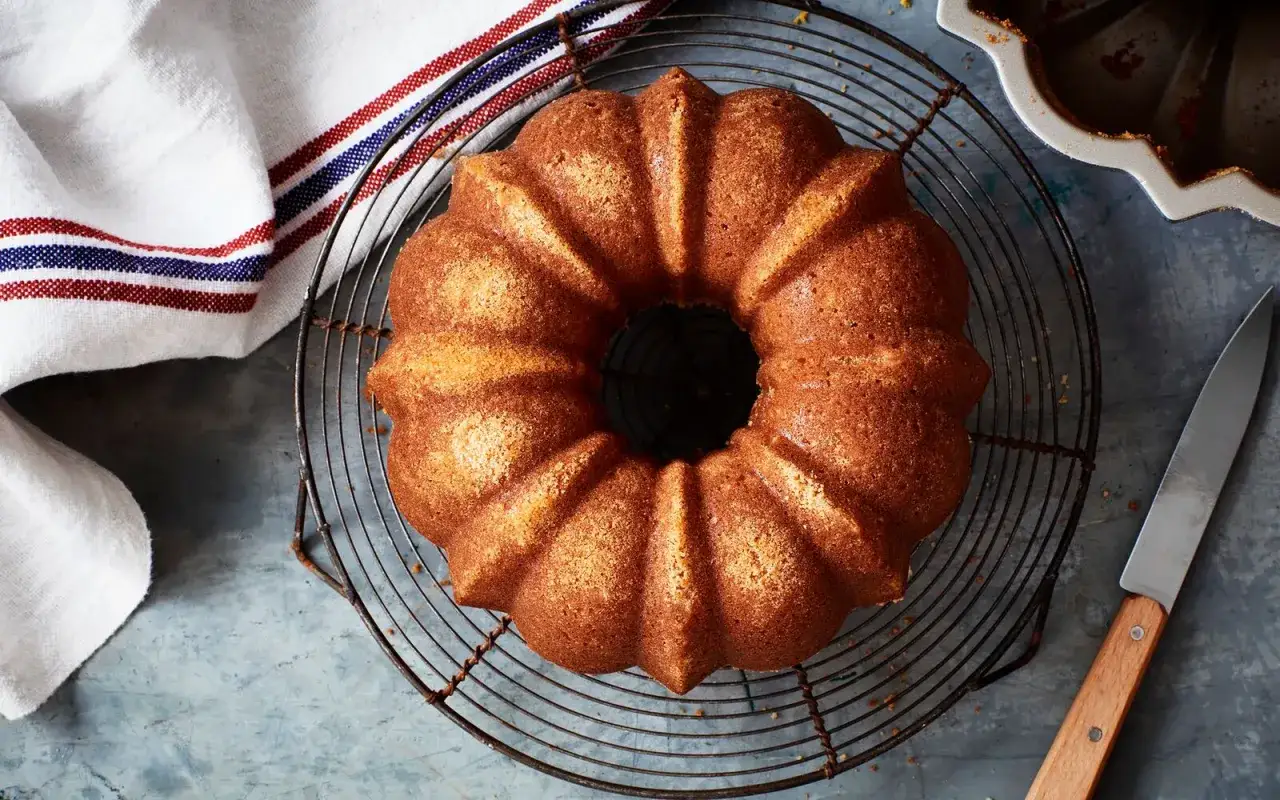 En gyllene sockerkaka med ett hål i mitten, perfekt för ett enkelt sockerkaka recept. Ligger på ett galler med en kökshandduk och kniv.
