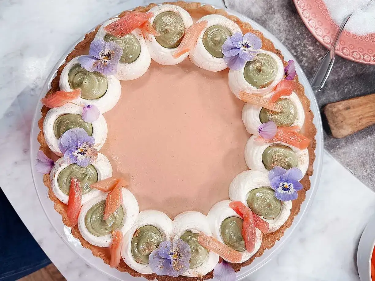 En vacker pannacotta med rabarber, dekorerad med vispad gr&auml;dde, pistagekr&auml;m och violer. En h&auml;rlig dessert f&ouml;r alla hj&auml;rtans dag.