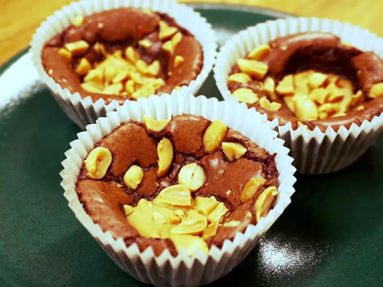 Tre chokladbrownies i pappersformar, toppade med jordnötter. Perfekt att baka med jordnötter för en härlig smak.