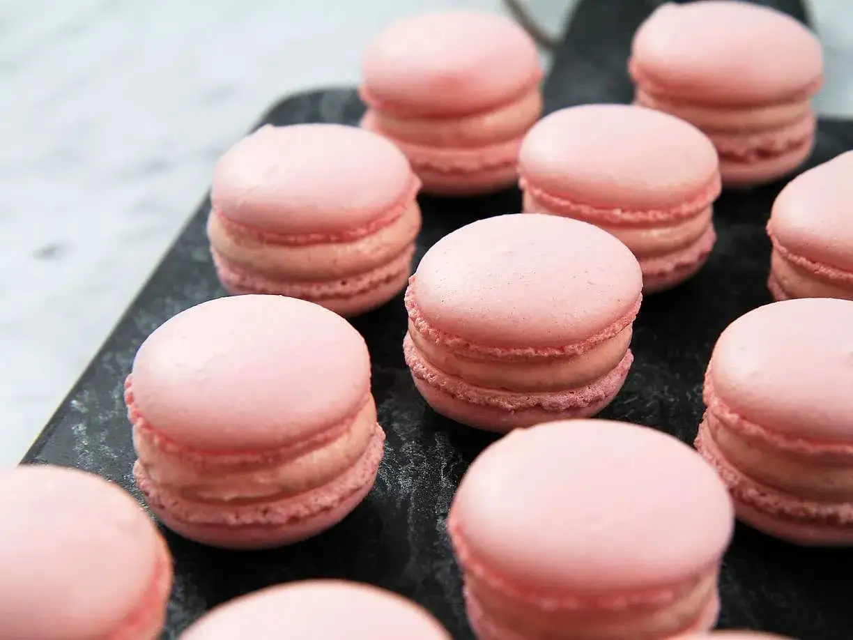 Rosa macarons p&aring; en m&ouml;rk yta, perfekta f&ouml;r ett macarons recept.