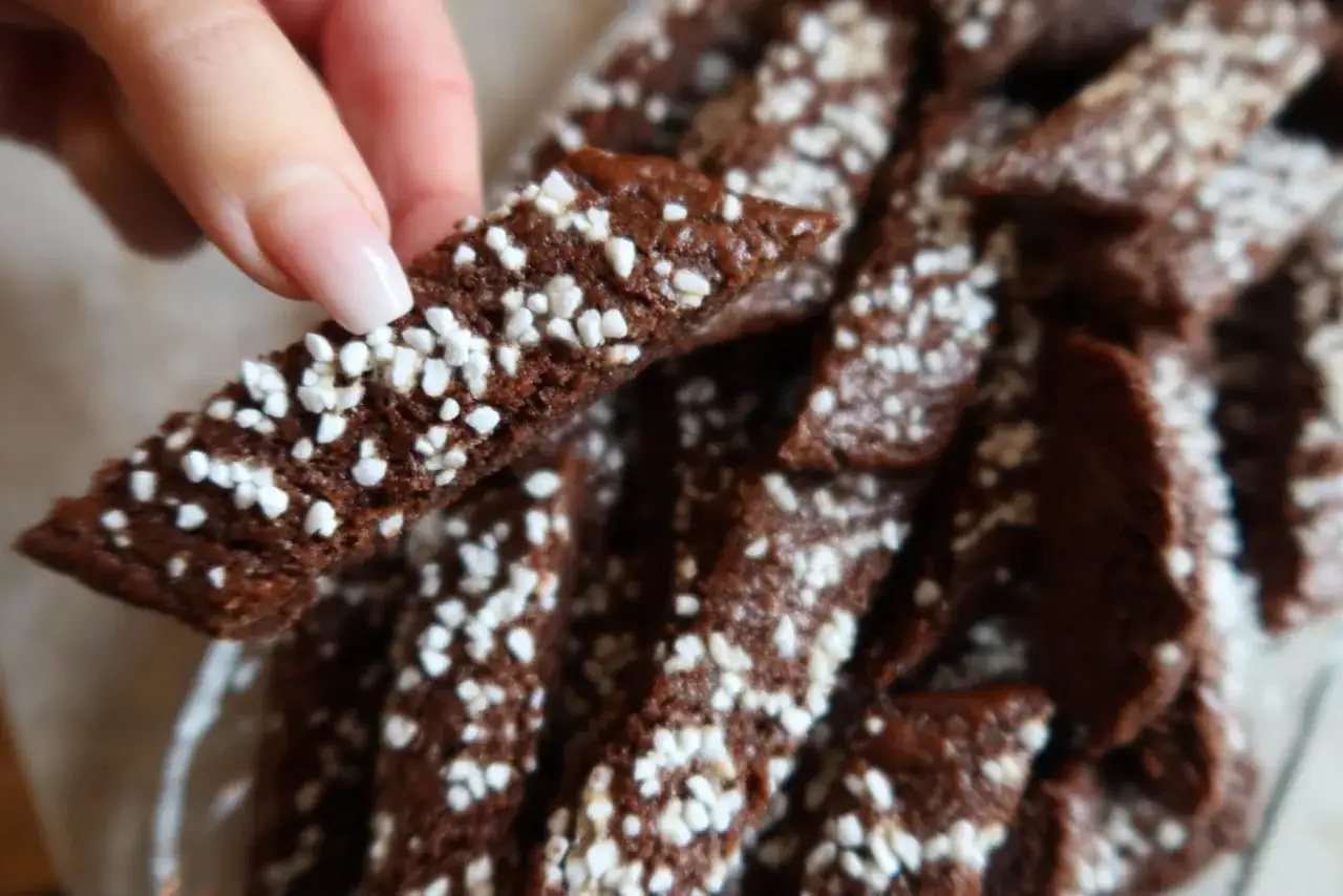 En hand h&aring;ller en chokladsnitt. Dessa sm&aring;, m&ouml;rka kakor &auml;r str&ouml;sslade med vita p&auml;rlsocker, perfekta f&ouml;r ett chokladsnittar recept.