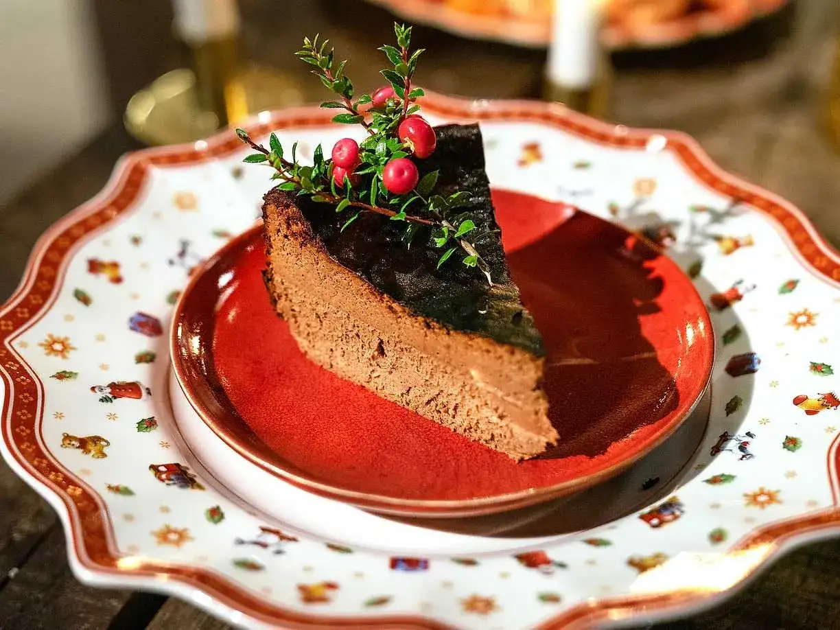 En bit kr&auml;mig choklad cheesecake med en glansig yta och dekorerad med lingonris. Serverad p&aring; en vacker jultallrik.