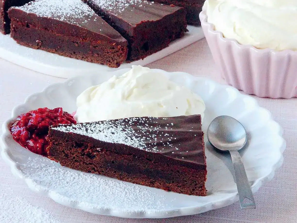 En bit fransk chokladt&aring;rta med vispad gr&auml;dde och hallonsylt. Pudrad med florsocker.
