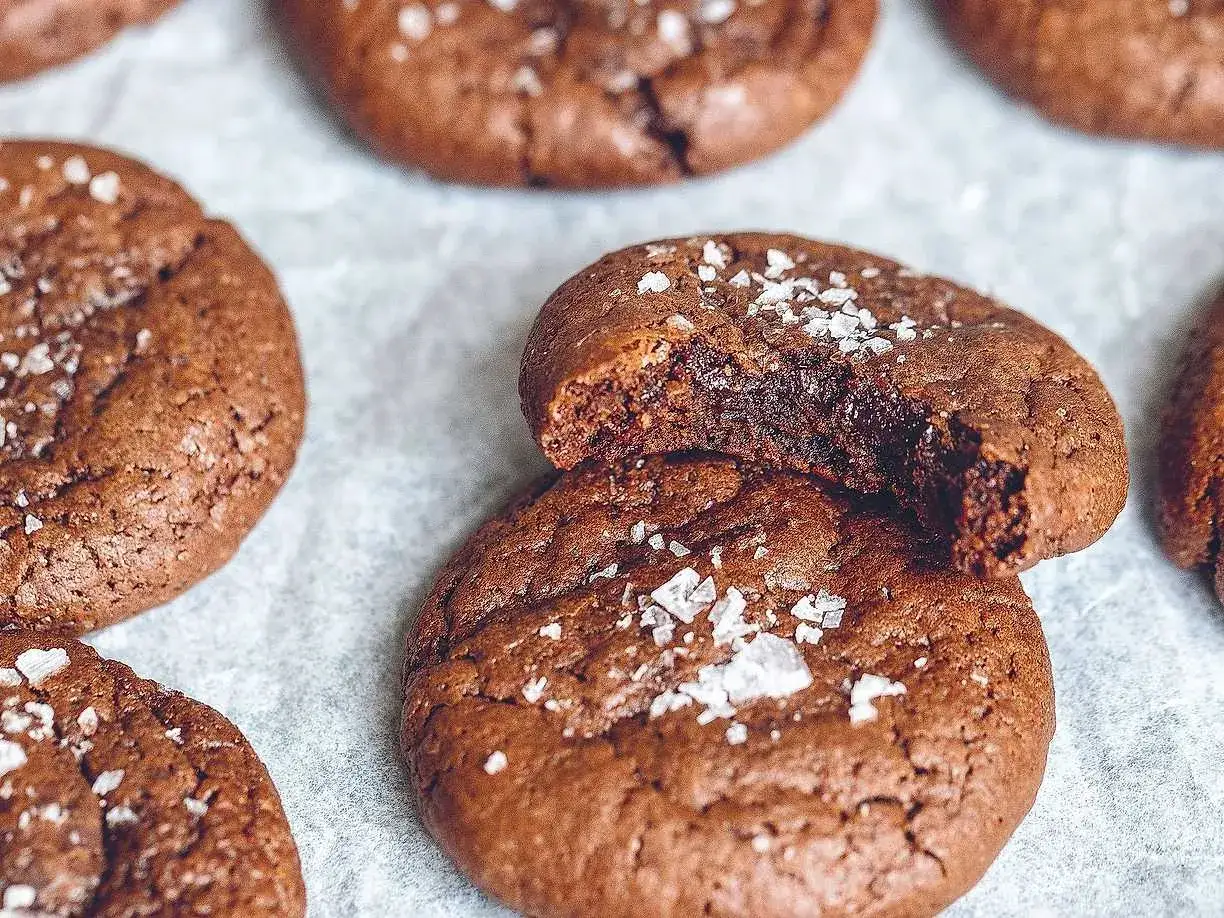 M&ouml;rka, sega kladdkake cookies toppade med flingsalt. En av dem &auml;r upp&auml;ten, vilket avsl&ouml;jar den h&auml;rliga kladdiga insidan.