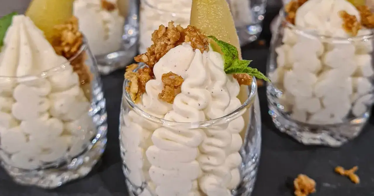 Vackert upplagd vispad pannacotta i glas, toppad med krispiga nötter och en bit päron. En elegant dessert.